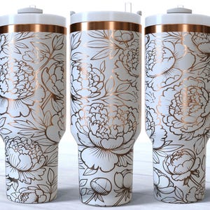 Puede incluir: Tres vasos de acero inoxidable con fondo blanco y un patrón floral dorado. Los vasos tienen una tapa y un asa.