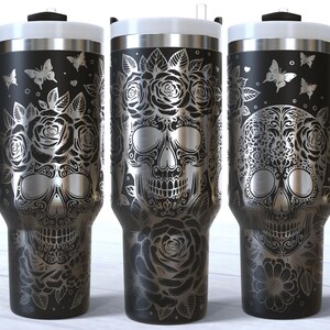 May include: Three black stainless steel travel mugs with a white sugar skull design. The skulls are adorned with floral patterns and butterflies.
