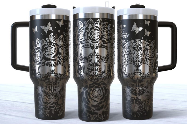 May include: Three black stainless steel travel mugs with a white sugar skull design. The skulls are adorned with floral patterns and butterflies.
