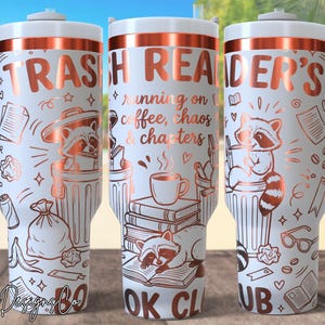 Op de afbeelding: Witte beker met een koperkleurig ontwerp met wasberen, vuilnisbakken, boeken en koffiekopjes. De tekst luidt "TRASH READER'S" en "running on coffee, chaos & chapters BOOK CLUB". De beker heeft een witte handgreep en deksel.