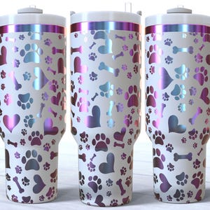 May include: Three stainless steel travel mugs with a white background and a pattern of pink and blue paw prints, hearts, and bones. The mugs have a silver lid and a handle.