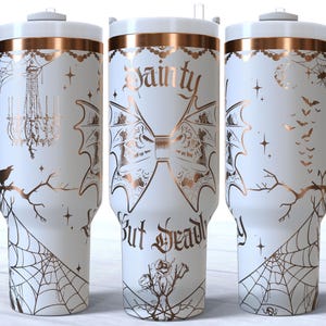 May include: White stainless steel tumbler with a rose gold design. The tumbler features a spiderweb pattern, bats, and the text "Dainty But Deadly".