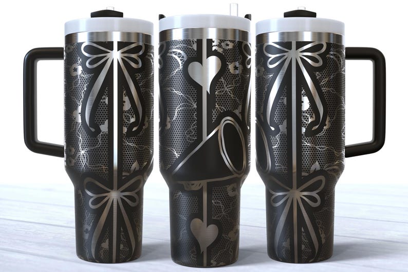 May include: Three stainless steel tumblers with black and silver designs. The tumblers have a black and silver lace pattern with a bow at the top and bottom. The middle tumbler has a heart and a black and silver design.
