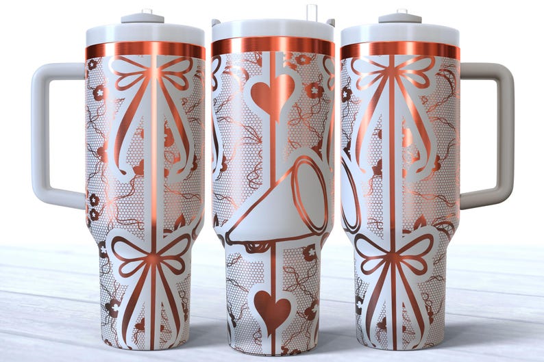 May include: Three stainless steel tumblers with a white background and a copper-colored design. The design features a bow, hearts, and a lace pattern.