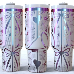 May include: Three stainless steel tumblers with a white background and a pink, purple, and blue iridescent design. The tumblers have a white bow and a white heart design. The tumblers have a handle.