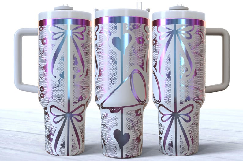 May include: Three stainless steel tumblers with a white background and a pink, purple, and blue iridescent design. The tumblers have a white bow and a white heart design. The tumblers have a handle.