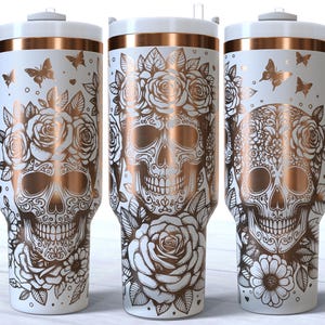 May include: Three white stainless steel tumblers with rose gold accents. Each tumbler features a detailed sugar skull design with floral accents and butterflies.