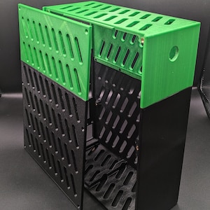 Könnte beinhalten: Eine schwarz-grüne 3D-gedruckte Box mit abnehmbarem Frontpanel. Die Box hat ein Gittermuster auf allen Seiten und ein rundes Loch oben.