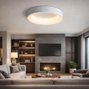 Puede incluir: Una moderna lámpara de techo circular blanca que emite una luz cálida y difusa. La lámpara está montada en un techo blanco. La habitación cuenta con una chimenea, un televisor grande y un sofá de tonos neutros, creando un espacio habitable acogedor.