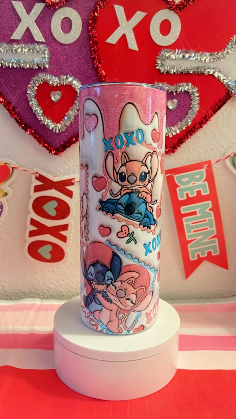 May include: Pink and white tumbler with a glitter finish featuring a cartoon couple of Stitch and Angel from the Disney movie Lilo & Stitch. The tumbler has a variety of hearts, flowers, and the words "XOXO" and "Be Mine" printed on it.
