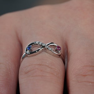 May include: A silver infinity ring with a row of clear cubic zirconia stones and two small gemstones, one blue and one pink.