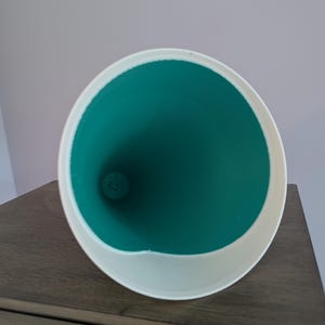 May include: A conical funnel with a smooth white exterior rim and a vibrant teal interior. The object features a wide circular opening that tapers down to a narrow circular base, showcasing a clean, minimalist design with a high-contrast color scheme.
