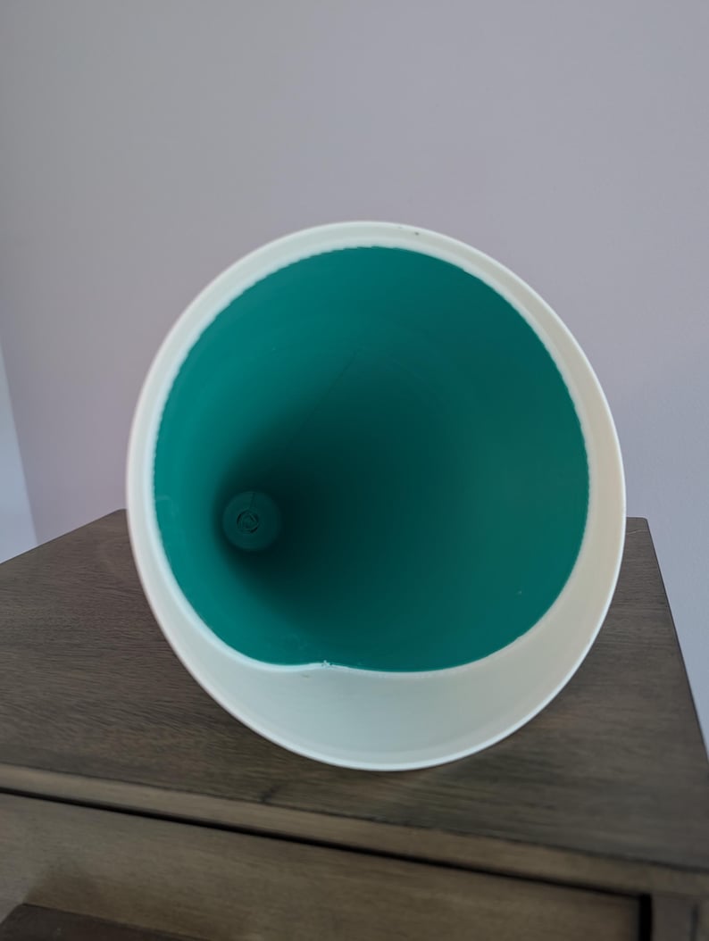 May include: A conical funnel with a smooth white exterior rim and a vibrant teal interior. The object features a wide circular opening that tapers down to a narrow circular base, showcasing a clean, minimalist design with a high-contrast color scheme.