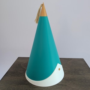 May include: A conical object featuring a teal body, a gold-colored pointed top, and a white base trim. A small gold-colored tassel hangs from the apex of the cone, and a single gold-colored circular stud is attached to the white base section.