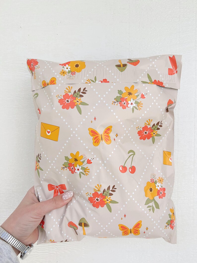 May include: A beige poly mailer with a repeating pattern of white polka dots, orange and yellow flowers, butterflies, cherries, and mushrooms. The mailer has a white seam down the center.