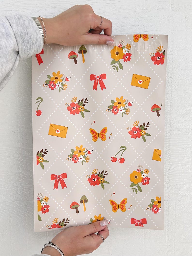 May include: A beige mailing envelope with a repeating pattern of red bows, yellow flowers, green leaves, red cherries, orange butterflies, and brown mushrooms. The envelope has a white dotted background.