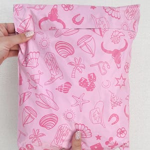 May include: Pink poly mailer with a repeating pattern of pink and white illustrations of various summer and western themed icons, including palm trees, seashells, horseshoes, and cacti.