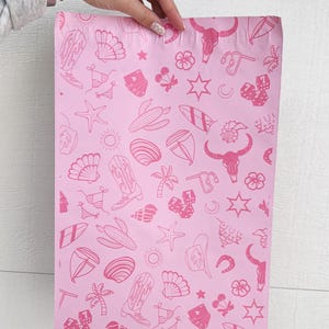 May include: Pink poly mailers with a repeating pattern of pink cowboy boots, seashells, surfboards, stars, cacti, and other western and beach themed icons.