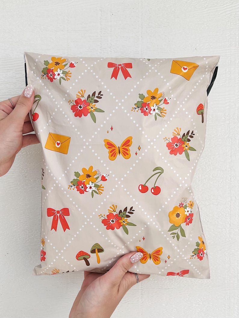May include: A beige poly mailer with a repeating pattern of red, yellow, and orange flowers, butterflies, cherries, mushrooms, and envelopes with hearts. The mailer has a white polka dot pattern and a diamond pattern.