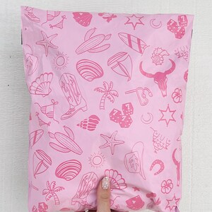 May include: Pink poly mailer with a repeating pattern of pink line drawings of various icons including a cactus, a surfboard, a cowboy boot, a seashell, a palm tree, a horseshoe, a star, a crescent moon, and dice.