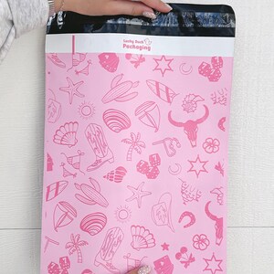 May include: Pink poly mailer with a white border and a repeating pattern of pink line drawings of various objects, including stars, palm trees, surfboards, seashells, cowboy boots, dice, and a bull skull. The text "Lucky Duck Packaging" is printed in white at the top of the mailer.
