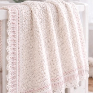 May include: A cream-colored crochet baby blanket with a pink border and scalloped edge is draped over a white crib. The text "Crochet Baby Blanket Pattern" is visible in the image.