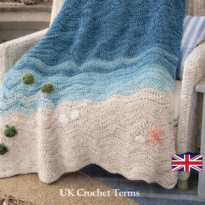 Può includere: Una coperta all'uncinetto a onde nei toni del blu e del crema, drappeggiata su una sedia di vimini. La coperta presenta un motivo a onde strutturato ed è decorata con elementi decorativi come conchiglie e una stella marina. Il testo recita "Wave Blanket Pattern (PDF)".