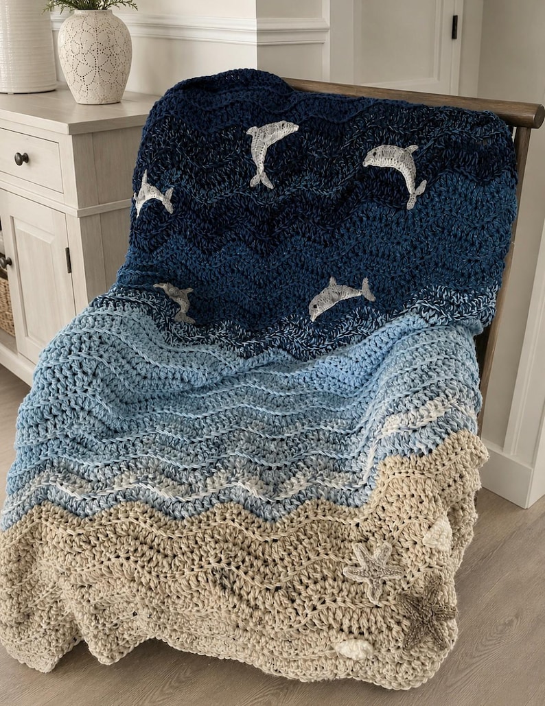 May include: A handmade crochet blanket in shades of blue and tan, depicting an ocean scene. The blanket features a wave pattern with embroidered dolphins and starfish. The blanket is draped over a wooden chair, showcasing its texture and design.