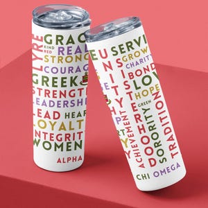 May include: Two white stainless steel tumblers with colourful text. The text on the left tumbler reads "GRACE REAL KIND RED STRONG COURAGE GREEK STRENGTH LEADERSHIP EAD HEAR LOYALT INTEGRIT WOMEN ALPHA". The text on the right tumbler reads "TRUE SERVI IN SGROW CHARIT N IBOND ETSLOV YTHOPE GREEN TRADITION ACHIEVEMENT SORORITY TH Y Y CHI OMEGA".