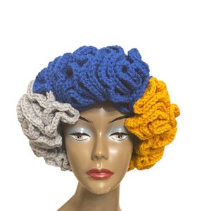 May include: A blue, grey, and yellow crocheted hat with a unique, textured design. The hat is made of soft yarn and has a comfortable fit.