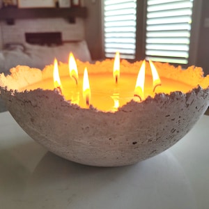 May include: A white concrete bowl with a rough texture filled with melted wax and multiple burning candles.