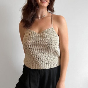 Op de afbeelding: Een beige gehaakt tanktop met een ronde hals en dunne bandjes. Het topje is gemaakt met een delicaat steekpatroon en heeft een ontspannen pasvorm.