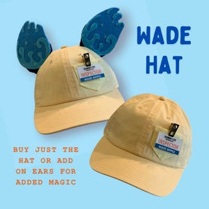 May include: Two light yellow baseball caps, one with blue water-like ears attached. Each cap has a small pocket with "ELEMENT CITY INSPECTOR WADE RIPPLE" text. The image also includes the text "WADE HAT" and "BUY JUST THE HAT OR ADD ON EARS FOR ADDED MAGIC."