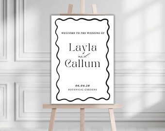 May include: A white wedding sign with a black wavy border. The text reads "Welcome to the wedding of Layla and Callum 06.04.28 Botanical Gardens".
