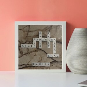 May include: A white square frame with a marble background and a Scrabble tile crossword puzzle spelling out the names Samantha, Kylie, Brad, and the word "family".