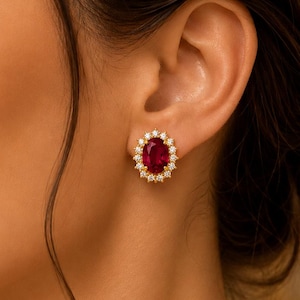 May include: Gold stud earrings featuring an oval ruby surrounded by a halo of small diamonds. The earrings are a classic design, suitable for adding a touch of elegance. The ruby is a deep red, and the diamonds provide extra sparkle. A timeless piece of jewellery.