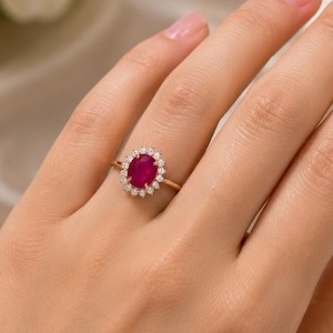 May include: A gold ring with an oval ruby centre stone, encircled by a halo of small diamonds. The ring's delicate gold band highlights the ruby's rich red hue and the diamonds' brilliance. A classic and elegant piece of jewellery.