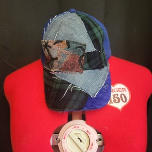 May include: A blue, denim, and plaid baseball cap with a patchwork design. The cap has a curved brim and a sewn-on patch with a floral pattern.