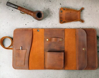 May include: A brown leather carrying case with multiple pockets and compartments, open to reveal the interior. The case has a strap and is designed to hold a pipe, tobacco, and other accessories.