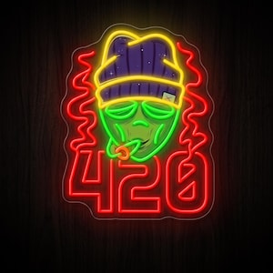 Op de afbeelding: Een neonbord met een groen alienhoofd dat een paarse muts met een gele rand draagt. De alien rookt, met rode neon rookwolken aan beide kanten. Onder de alien staat het getal 420 weergegeven in felrode neonletters op het bord.