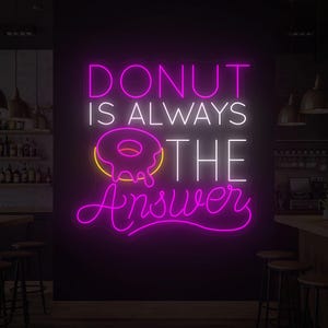 Peut inclure: Enseigne au néon rose et blanc avec l'inscription « DONUT IS ALWAYS THE Answer ». Le mot « DONUT » est en haut, avec un dessin de donut en dessous. L'enseigne est dans une pièce sombre, peut-être un café.