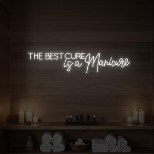 Könnte beinhalten: Ein weißes Neon-Schild mit dem Text "THE BEST CURE is a Manicure" hängt an einer Holzwand. Darunter befindet sich ein Regal mit gerollten Handtüchern, Kerzen und kleinen Flaschen, wodurch eine Spa-Atmosphäre entsteht.