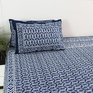 Op de afbeelding: Een beddengoedset met marineblauw en wit patroon met een gedetailleerd ontwerp. De set bevat een hoeslaken, een laken en twee kussenslopen. De kussenslopen en de rand van de lakens hebben een geometrisch ontwerp.