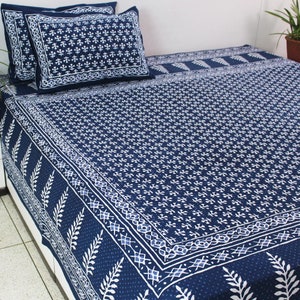 May include: A navy blue and white patterned bed set, including a fitted sheet and two pillowcases. The bedding features a repeating white floral design and a decorative border. The pillowcases are placed on top of the bed.
