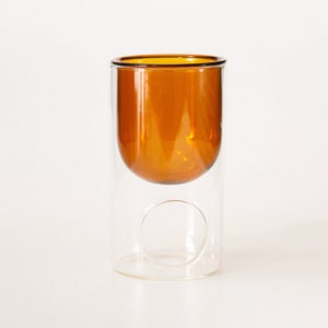 May include: A clear glass double-walled vase with an amber coloured glass inner layer. The vase has a circular opening in the bottom of the outer layer.