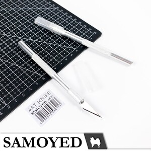 May include: Two silver art knives with black handles on a black cutting mat. The knives have a silver blade and a black label that reads "ART KNIFE SAMOYED AK-25" with a barcode.