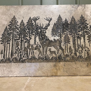 May include: A decorative tile featuring a black and white silhouette of a deer and two fawns standing in a forest. The tile has a light brown background.