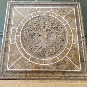 May include: A square tile with a beige background and white grout lines. The tile features a carved tree of life design in the center.