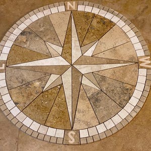 May include: A compass rose made of stone tiles in shades of brown and white. The compass points are labeled N, E, S, and W.