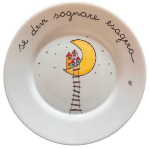 Può includere: Piatto in ceramica bianca con un disegno disegnato a mano. Il piatto presenta una luna crescente gialla con case colorate in cima, una scala e il testo italiano "se devi sognare esagera".